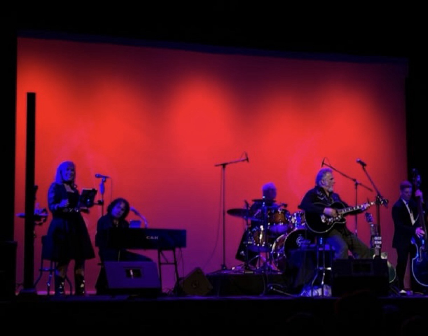 Steven Kent seated with the band on a red stage